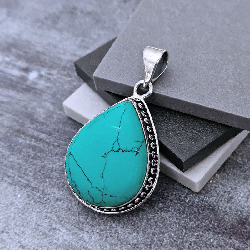 Teardrop-shaped Turquoise pendant set in sterling silver on a grey background