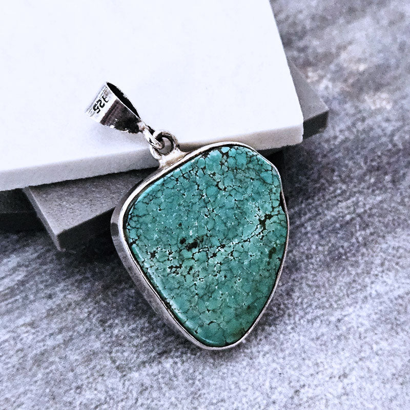 Turquoise pendant with silver frame on a textured surface