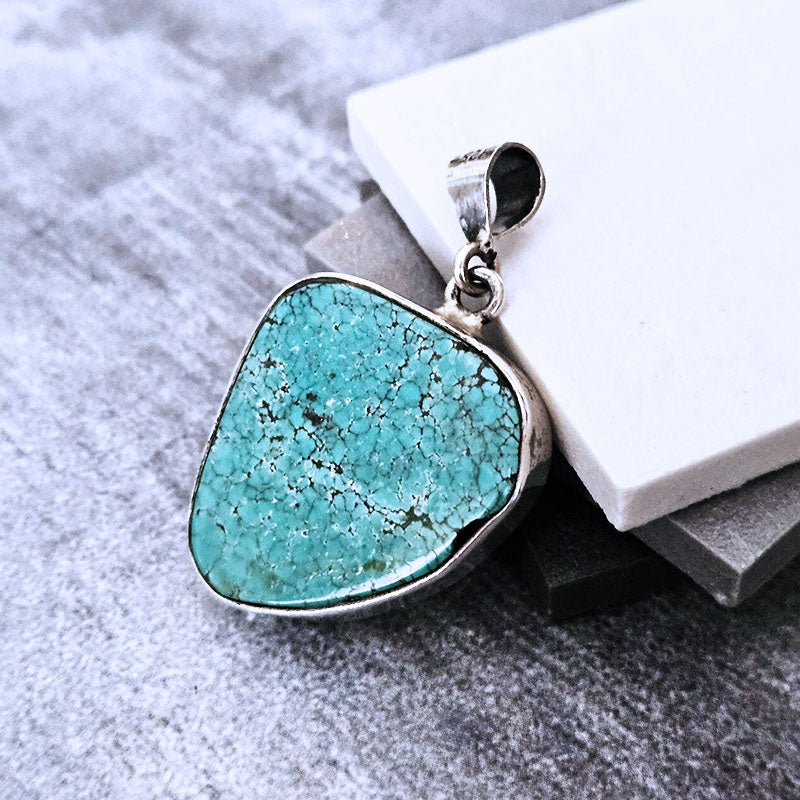 Turquoise pendant on a gray surface with a white stone in the background