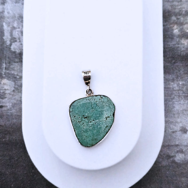 Green stone pendant on a white plate with a gray background