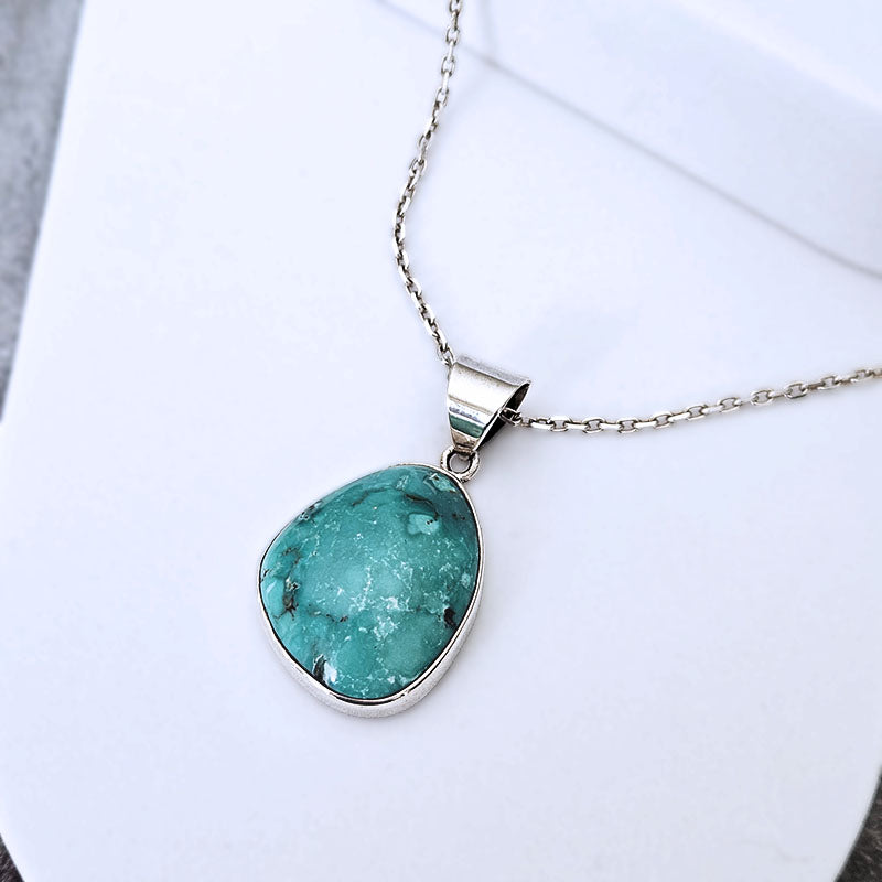 A silver pendant necklace featuring a teardrop-shaped turquoise stone with natural white and dark veining, displayed on a clean white surface.