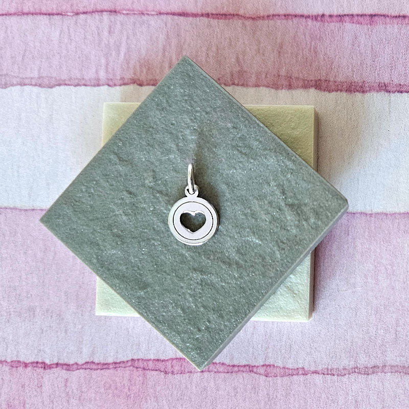 Silver heart-shaped pendant on a green card with a pink and white striped background