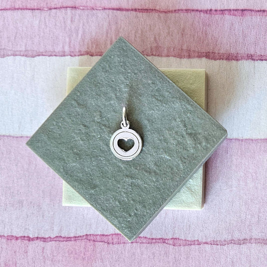 Silver heart-shaped pendant on a green card with a pink and white striped background