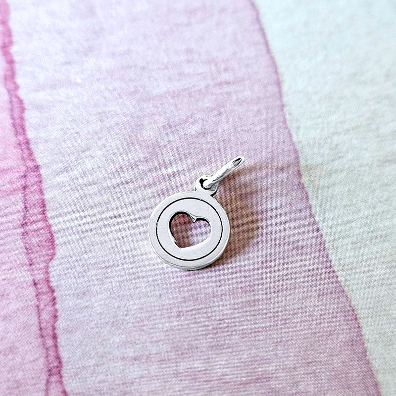 Silver pendant with a heart design on a textured pink and white background