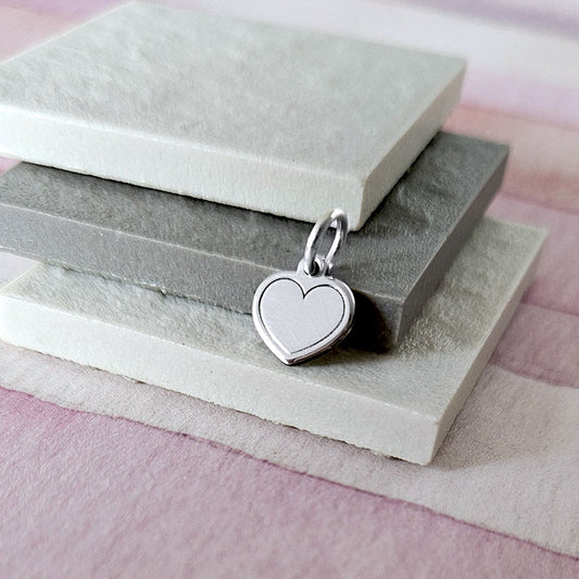 Silver heart-shaped pendant on a stack of stone blocks with a soft pink background