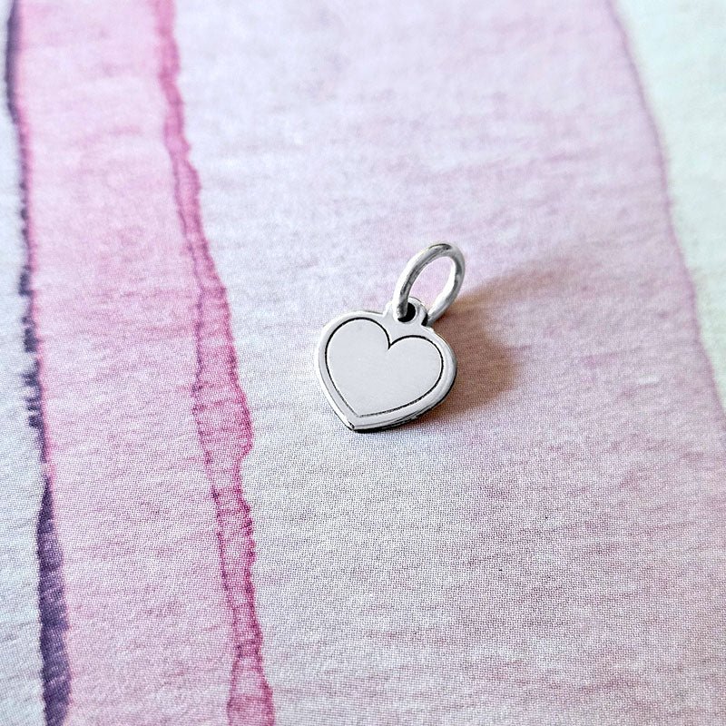 Silver heart-shaped pendant on a textured pink surface