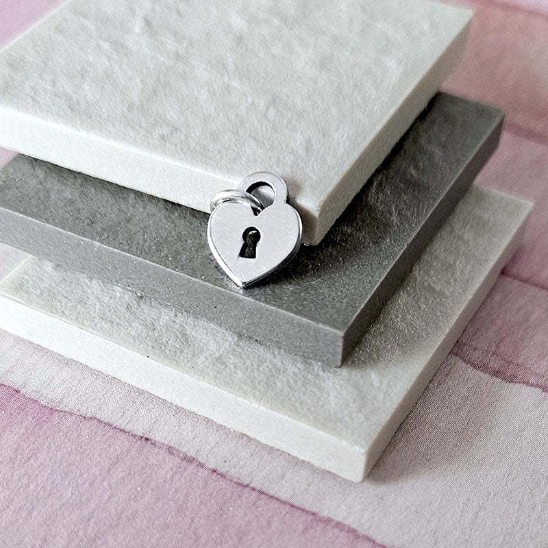 Silver heart-shaped padlock charm on a stack of gray and white stones.