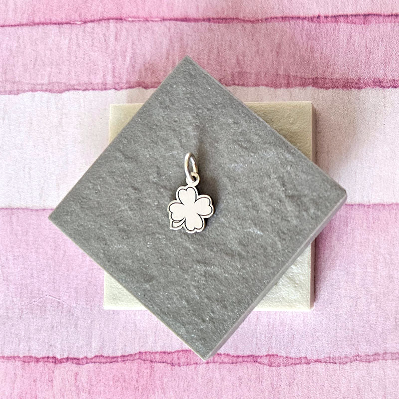 Silver four-leaf clover charm on a gray card with a pink striped background