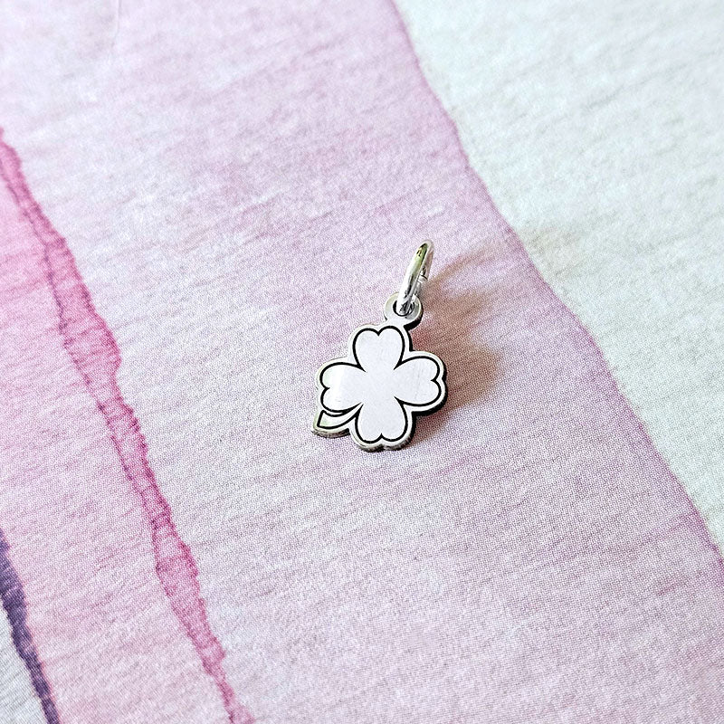 Silver four-leaf clover charm on a pink and white fabric background