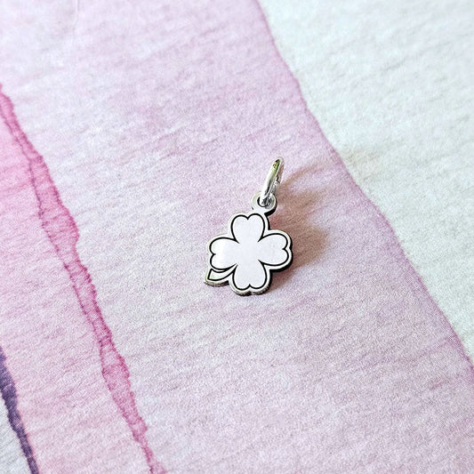 Silver four-leaf clover charm on a pink and white fabric background