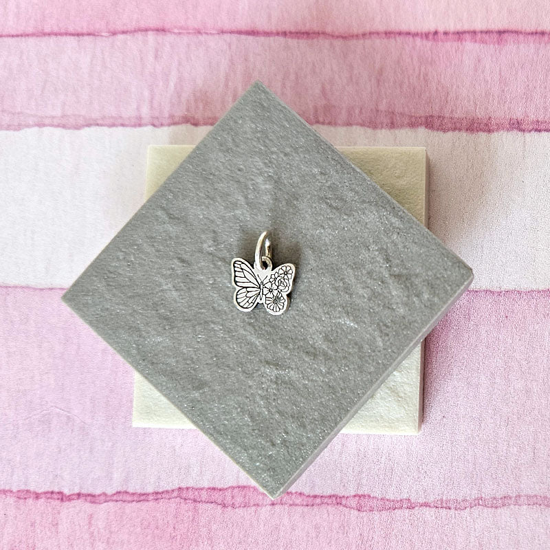 Silver butterfly charm on a gray card with a pink and white striped background