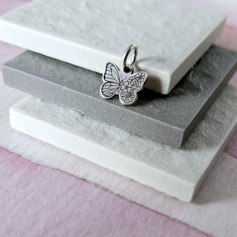 Silver butterfly charm on a stack of stone slabs with a pink background