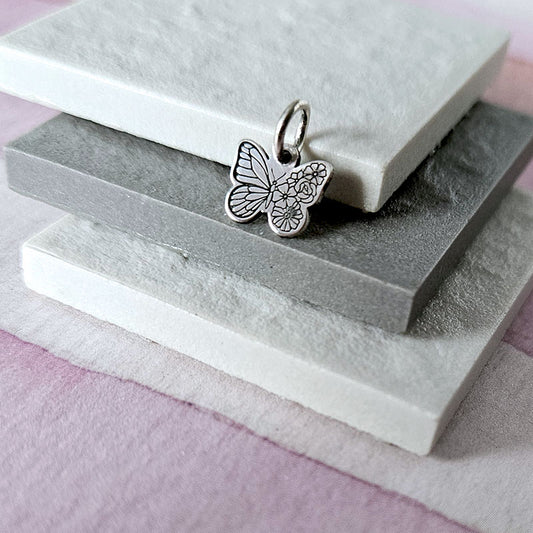 Silver butterfly charm on a stack of stone slabs with a pink background