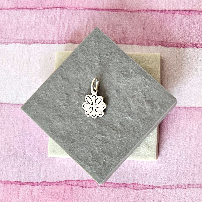Silver flower-shaped pendant on a gray card with a pink and white striped background