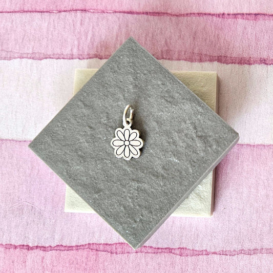Silver flower-shaped pendant on a gray card with a pink and white striped background