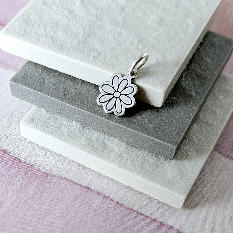 Silver flower pendant on a stack of stone blocks with a soft pink background