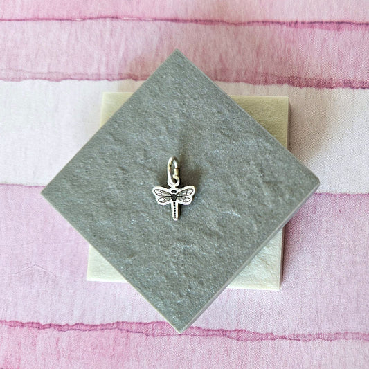 Silver dragonfly charm on a green card with a pink and white striped background