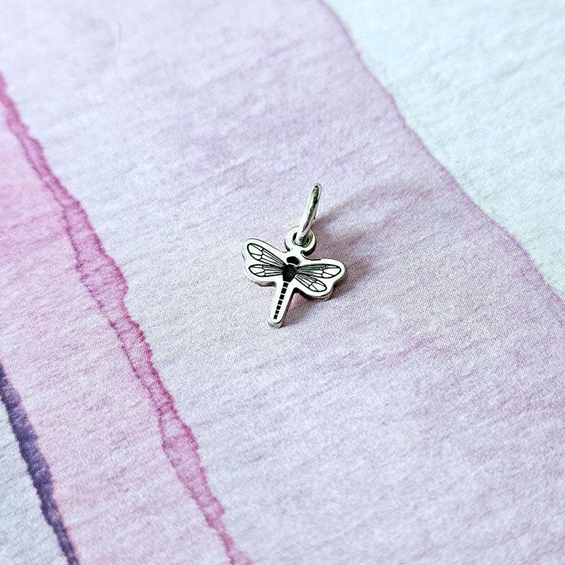Silver dragonfly charm on a pink and white textured background