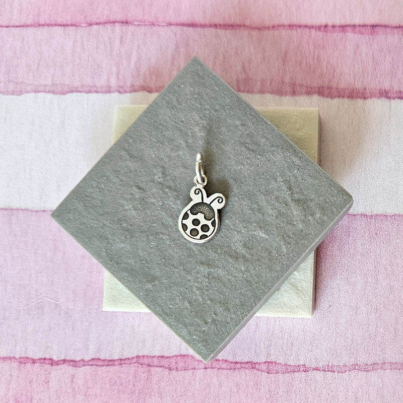 Silver ladybug pendant on a gray card with a pink and white striped background