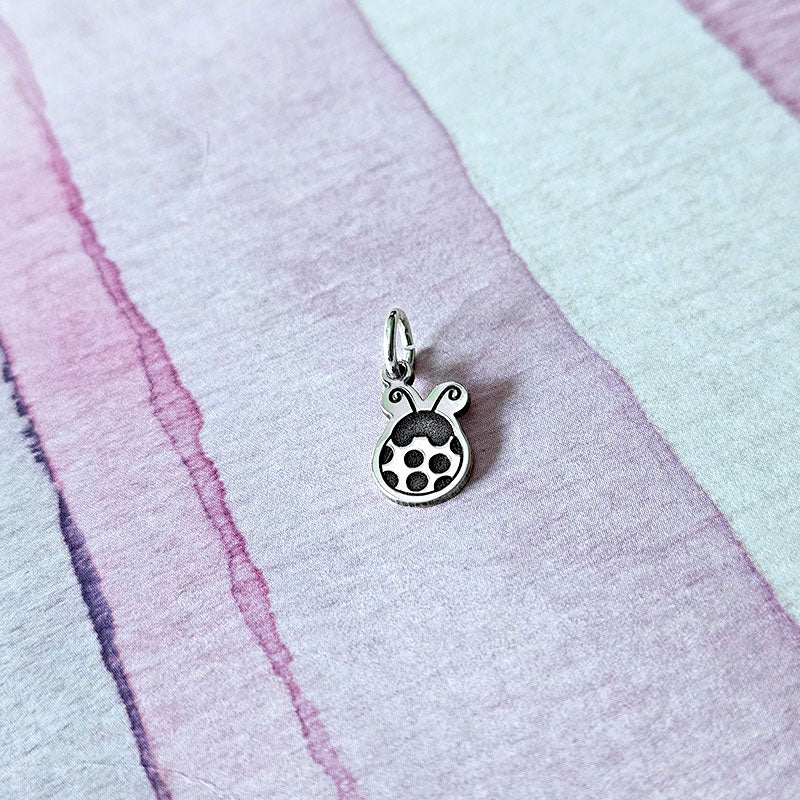 Silver  ladybug charm on a pastel striped fabric background