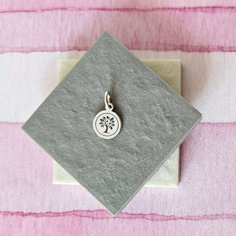 Silver tree pendant on a gray card with a pink plaid background