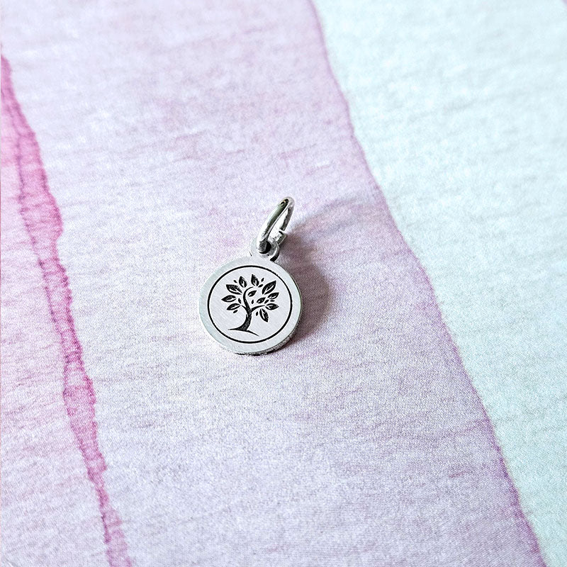 Silver tree pendant on a textured pink and white background