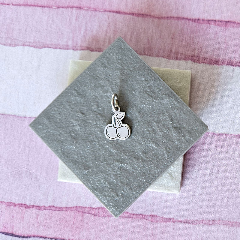 Silver cherry charm on a gray card with a pink and white striped background