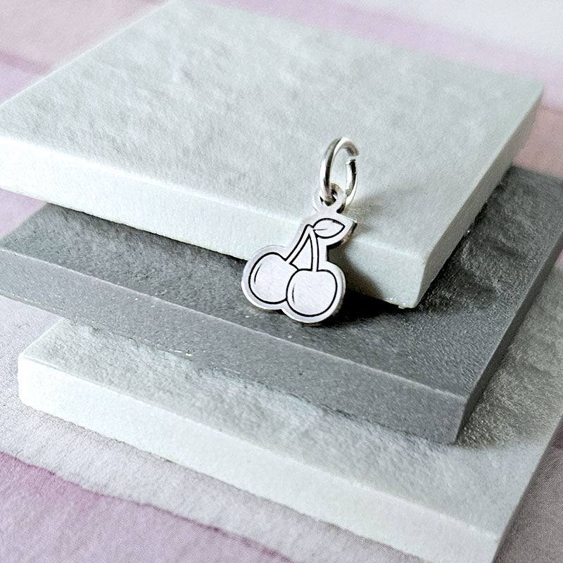 Silver cherry pendant on a stone surface with a soft pink background