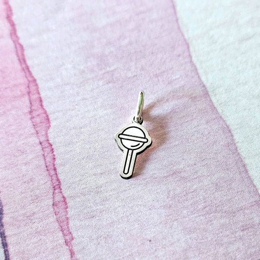 Silver charm resembling a lollipop on a textured pink surface