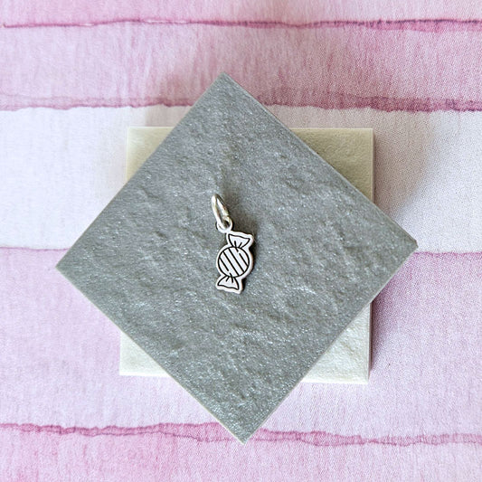 Silver candy-shaped charm on a gray card with a pink and white striped background