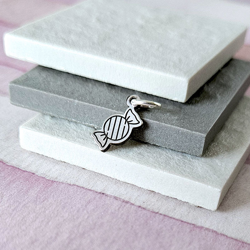 Silver candy-shaped pendant on a stack of gray stone slabs with a pink fabric background