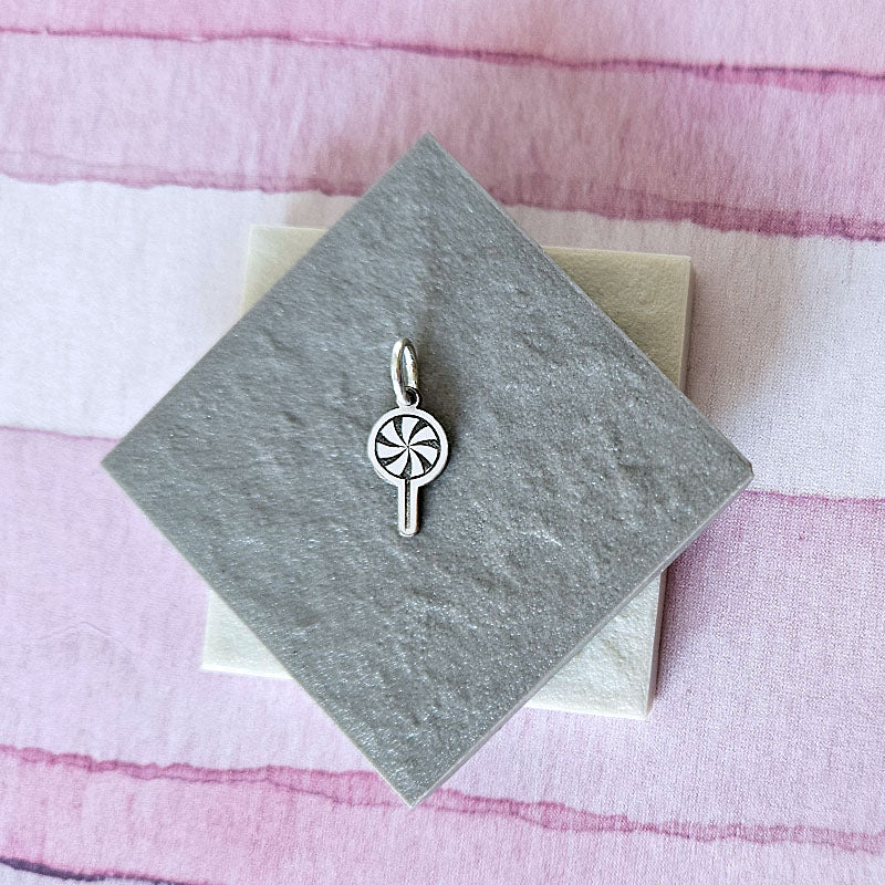 Silver pendant on a gray card with a pink striped background