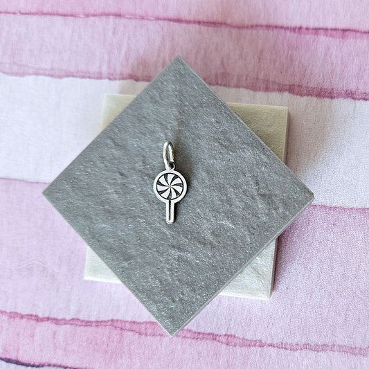 Silver pendant on a gray card with a pink striped background