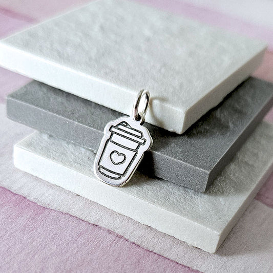 Silver pendant shaped like a coffee cup with a heart on a stone surface