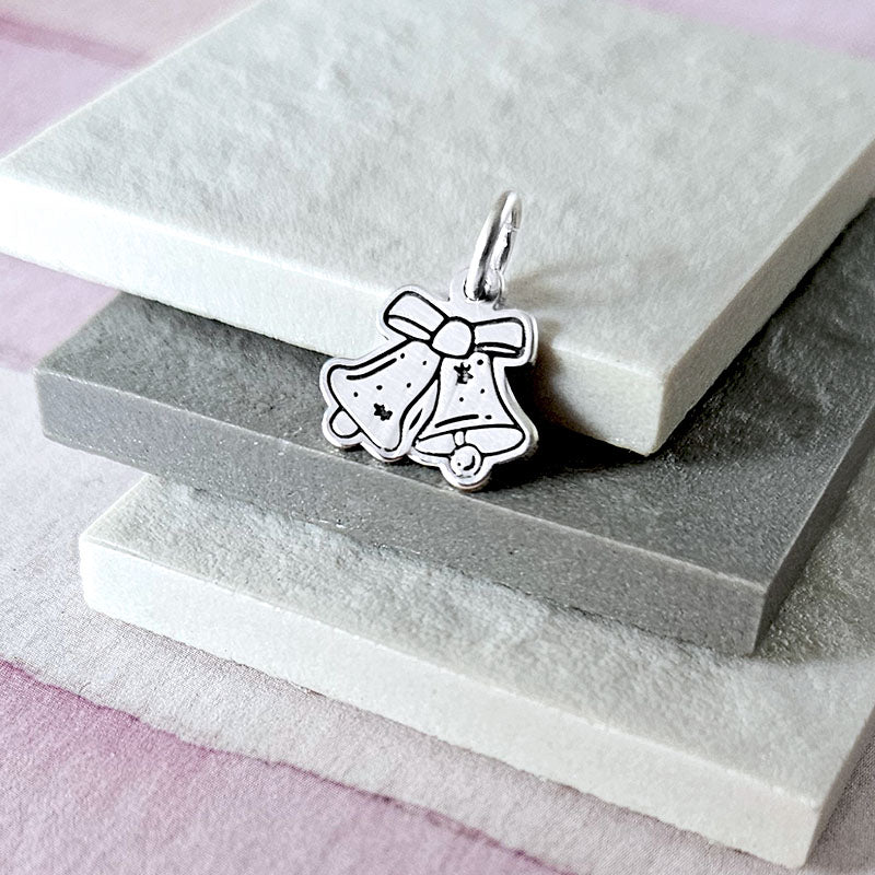 Silver bell charm with a bow on a gray stone surface