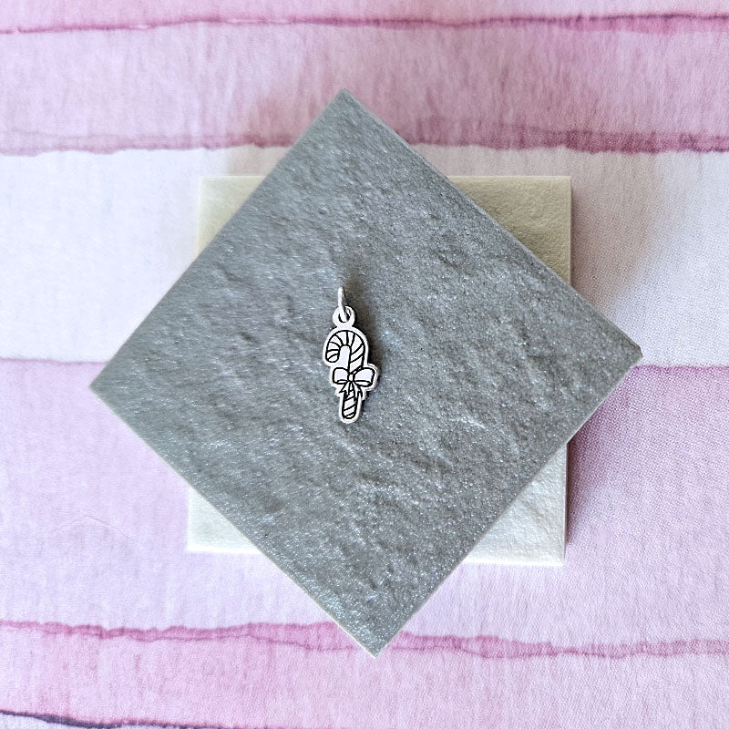 Silver candy cane charm on a gray card with a pink striped background