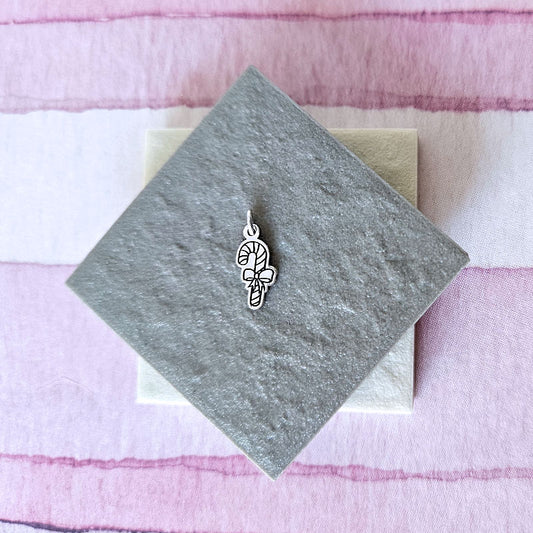 Silver candy cane charm on a gray card with a pink striped background