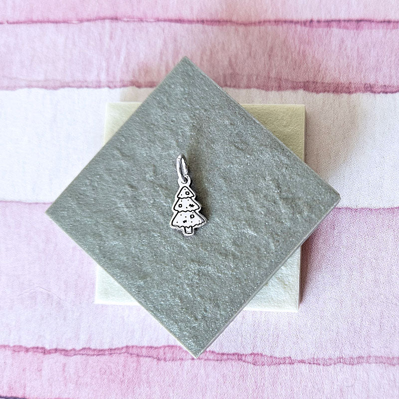 Silver Christmas tree charm on a gray card with a pink and white striped background