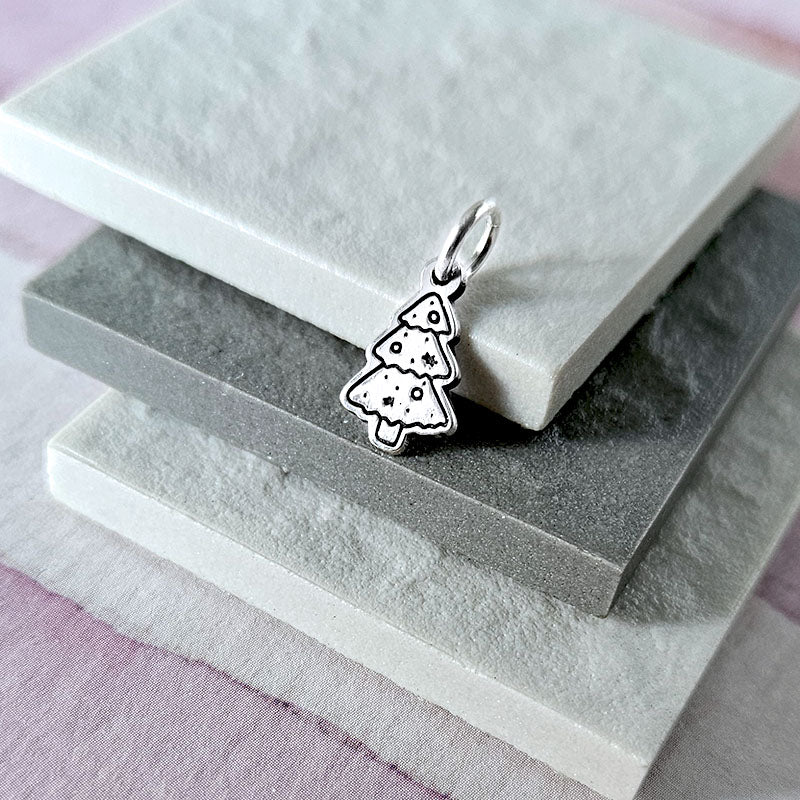 Silver Christmas tree charm on a stack of gray and white stones.
