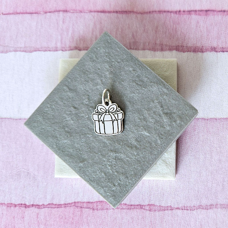 Silver gift box charm on a gray card with a pink and white striped background