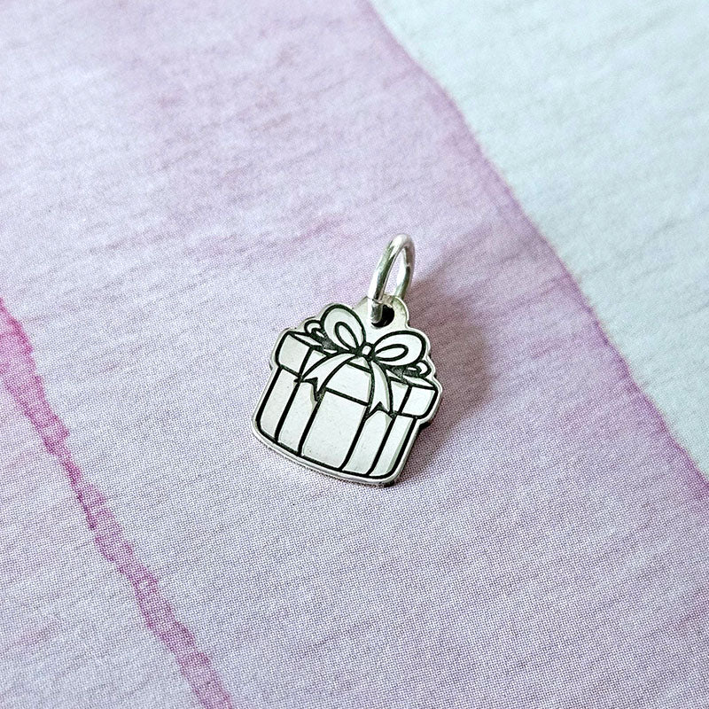 Silver gift box charm on a pink fabric background