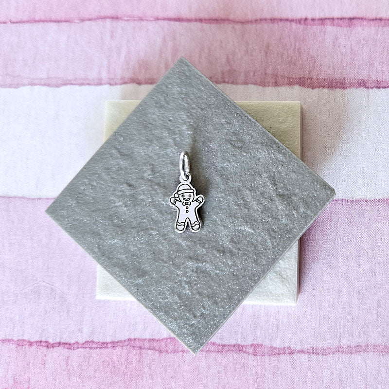 Silver gingerbread man charm on a gray card with a pink textured background
