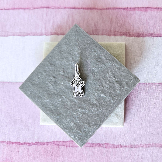 Silver gingerbread man charm on a gray card with a pink textured background
