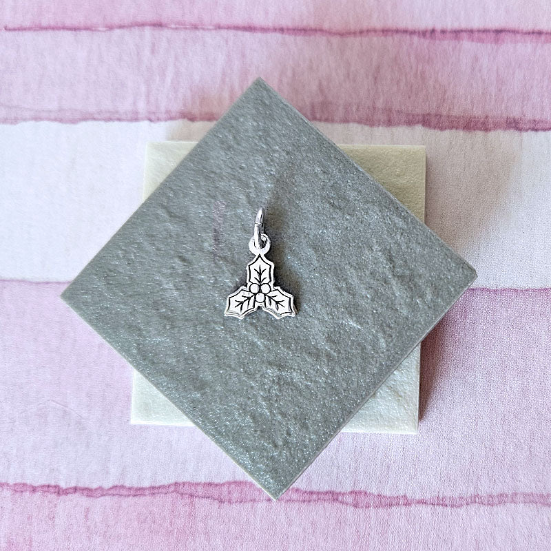 Silver pendant on a textured gray card with a pink and white striped background