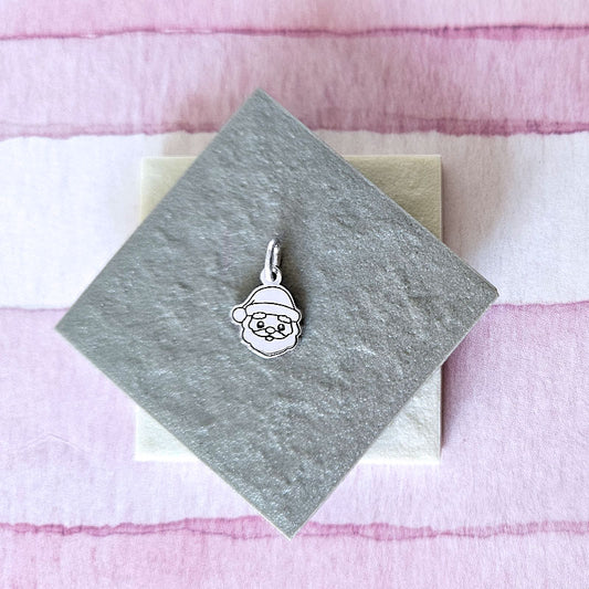 Silver pendant of a face with a Santa hat on a gray card with a pink and white striped background