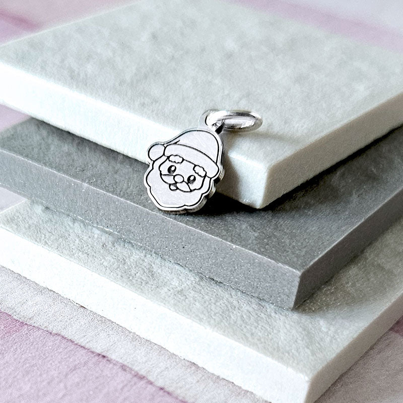 Silver pendant of a face with a Santa hat on a white stone surface