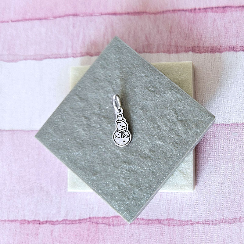 Silver snowman charm on a gray card with a pink and white striped background