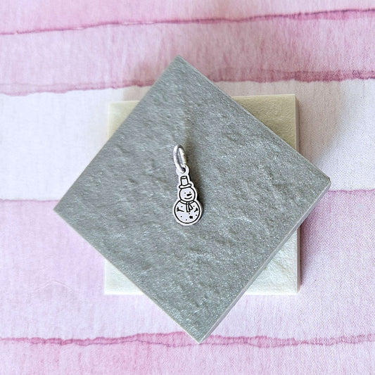 Silver snowman charm on a gray card with a pink and white striped background