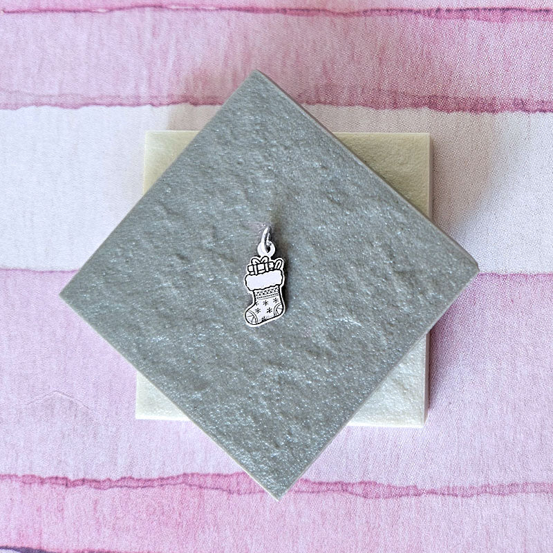 Silver stocking charm on a gray card with a pink striped background