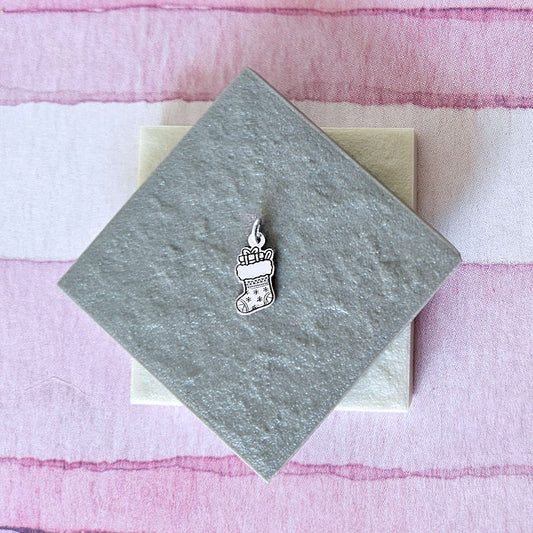 Silver stocking charm on a gray card with a pink striped background
